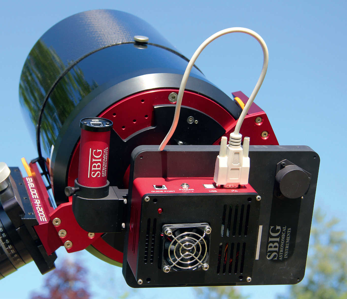 Une caméra CCD refroidie sur un astrographe : entre le tube et la caméra (boîtier rouge/noir), on voit la roue à filtres (également noire) et, à côté, une caméra de suivi ronde (rouge) reliée au chemin optique de la lunette via un Off-Axis-Guider. U. Dittler